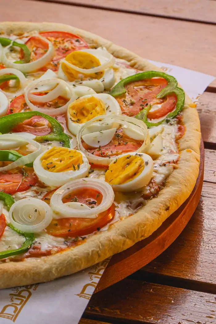 Mouth-watering pizza topped with eggs, onions, green peppers, and tomatoes served on a wooden table.