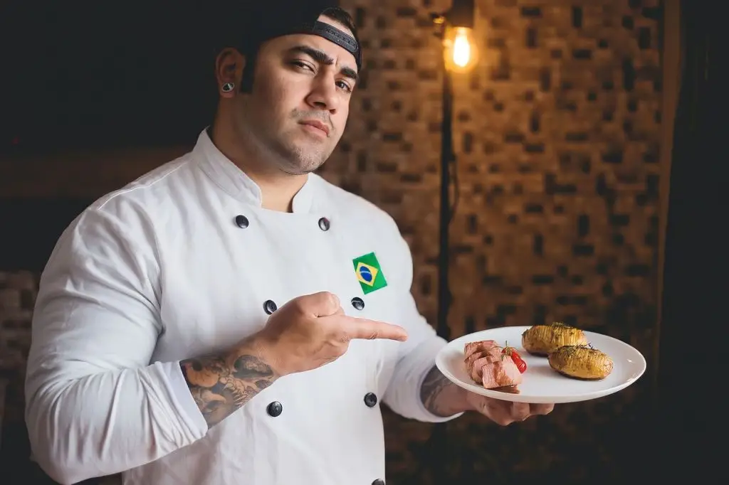 Chef in white uniform pointing at gourmet meal on plate, showcasing culinary skills.