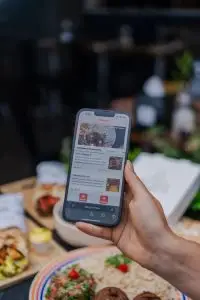 Hand holding a smartphone displaying a food delivery app screen in a restaurant setting.