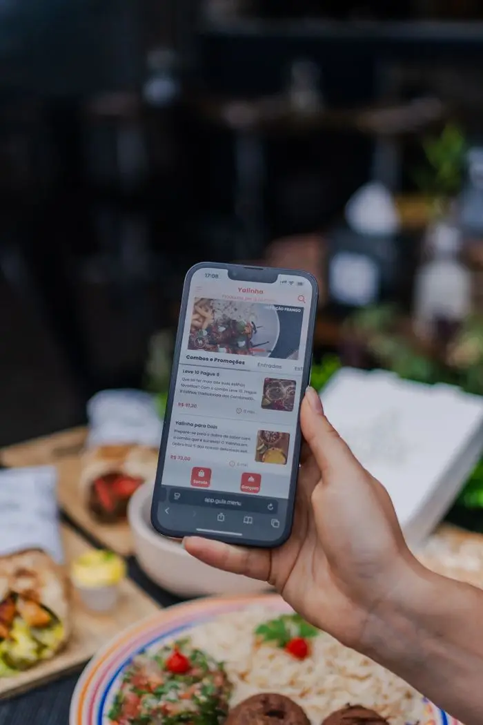 Hand holding a smartphone displaying a food delivery app screen in a restaurant setting.